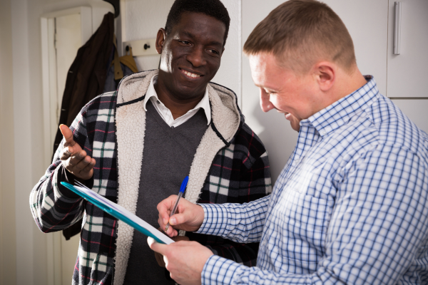 2 people looking at clipboard, smiling, one is writing on board